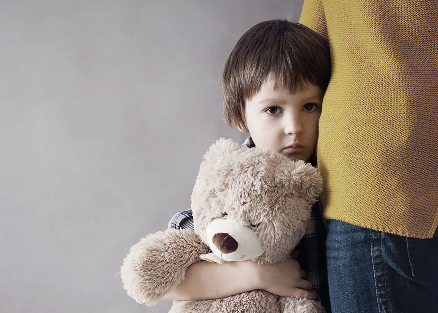 Child holding a teddy bear beside an adult