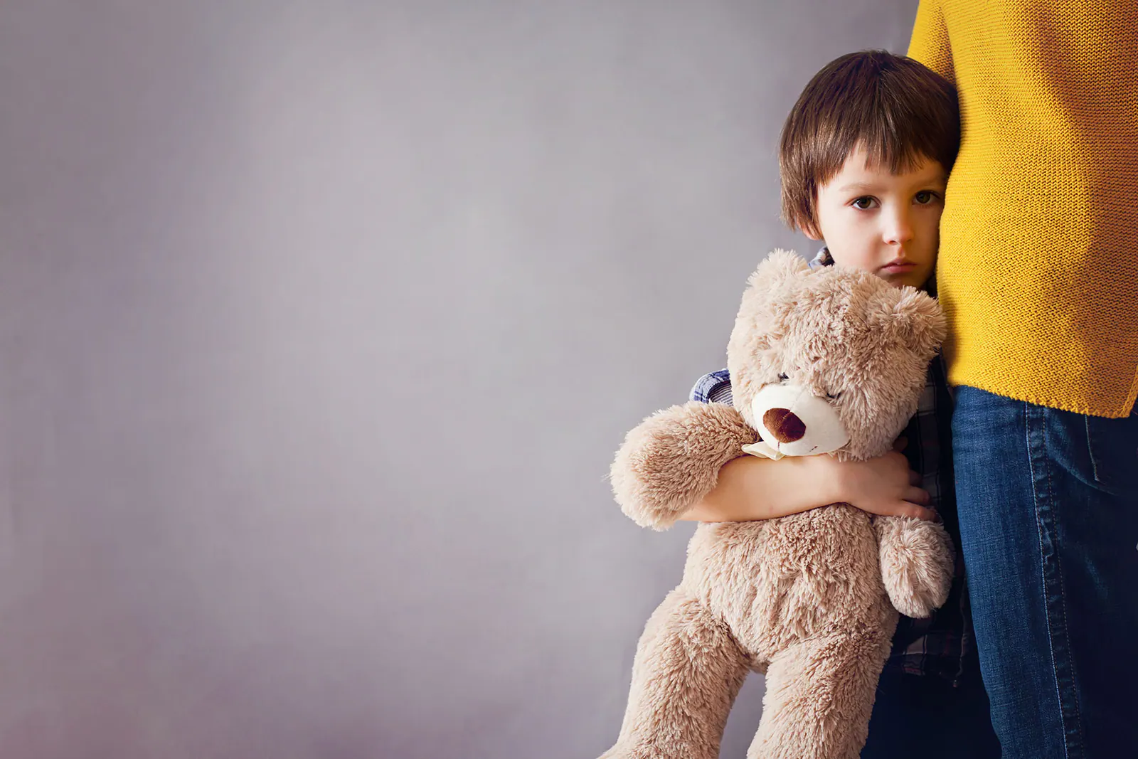 Child holding a teddy bear beside an adult